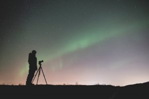 silhouette of person standing near a tripod under green sky with stars